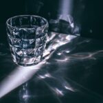 A glass tumbler casting intricate reflections and shadows on a surface.
