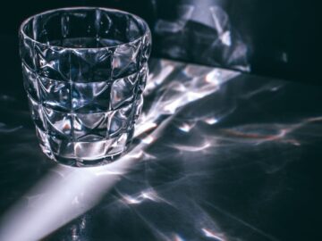 A glass tumbler casting intricate reflections and shadows on a surface.