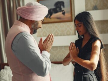 A Sikh father and daughter share a moment of meditation and cultural practice indoors.