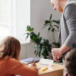 A teacher helps students during a classroom activity with books and notepads.