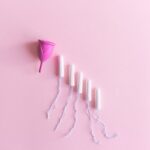 Top view arrangement of pink menstrual cup placed on light pink surface near tampons