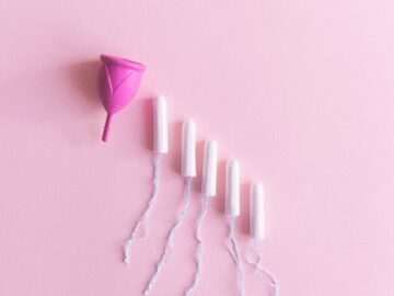 Top view arrangement of pink menstrual cup placed on light pink surface near tampons
