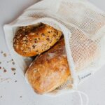 Close-up of assorted freshly baked bread in an eco-friendly net bag on a white surface.