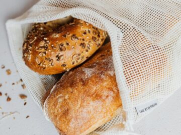 Close-up of assorted freshly baked bread in an eco-friendly net bag on a white surface.