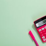 Pink calculator and pen on a pastel green background with copy space.