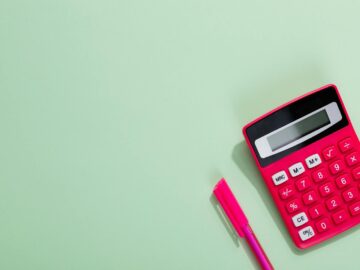 Pink calculator and pen on a pastel green background with copy space.
