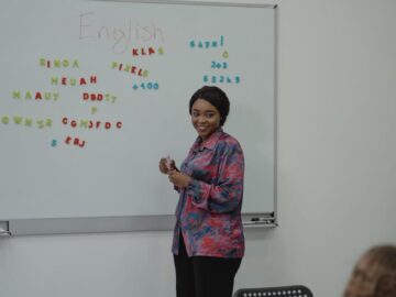 A female teacher explaining an English lesson to students in a classroom with a whiteboard.
