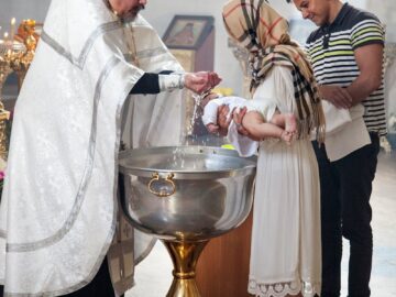 A priest performs a baptism ceremony on a baby in a church, witnessed by parents.