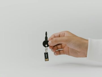 Hand holding keychain with integrated USB flash drive against a plain background.