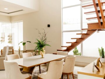 Interior of light living room with wooden stairs and table with comfortable chairs in contemporary house