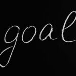 Elegant handwritten 'goal' on a black chalkboard background conveying ambition and purpose.