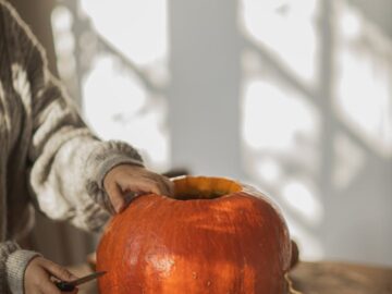 Person carving pumpkins indoors with warm sunlight on a fall day.
