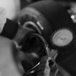 Black and white image of a mechanic using a gauge to check tire pressure on a kart wheel.