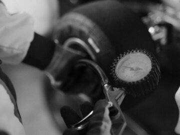 Black and white image of a mechanic using a gauge to check tire pressure on a kart wheel.