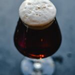 A close-up of a dark beer in a glass with a frothy head, showcasing the rich texture and color.