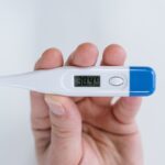 Close-up of a hand holding a digital thermometer showing a high fever reading of 38.4°C.