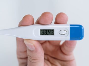 Close-up of a hand holding a digital thermometer showing a high fever reading of 38.4°C.