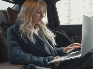 Businesswoman working remotely on a laptop in the backseat of a luxury car. Stylish, modern, and focused.