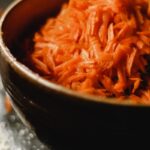 A close-up shot of freshly grated carrots in a rustic bowl, perfect for salads.