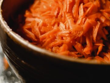 A close-up shot of freshly grated carrots in a rustic bowl, perfect for salads.