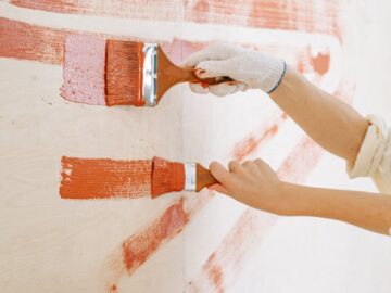 Close-up of hands painting a wall with red strokes, emphasizing DIY home renovation.