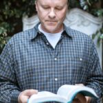 An adult man reads a Bible outdoors, exuding peace and contemplation in a serene setting.