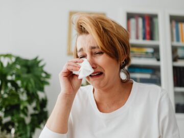 Woman crying over financial problems, surrounded by money indoors.
