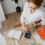 Top view of a woman managing finances with a calculator, cash, and bills in a home setting.