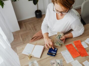 Top view of a woman managing finances with a calculator, cash, and bills in a home setting.