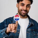 Portrait of a man in denim jacket smiling while holding 'I Voted Early' sticker.
