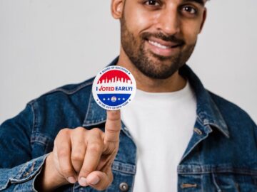 Portrait of a man in denim jacket smiling while holding 'I Voted Early' sticker.