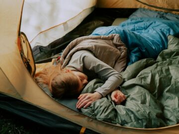 A serene scene of a woman sleeping comfortably in a tent during a camping trip, surrounded by nature.