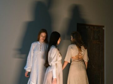 Three women engage in a mystical ritual, casting long shadows on the wall.