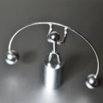 Stainless weightlifter kinetic perpetual dynamic motion toy with balance balls placed on gray table in light room on blurred background