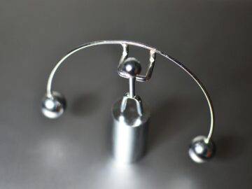 Stainless weightlifter kinetic perpetual dynamic motion toy with balance balls placed on gray table in light room on blurred background