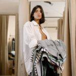 Woman stands in fitting room holding clothes and looking confident in a clothing store.