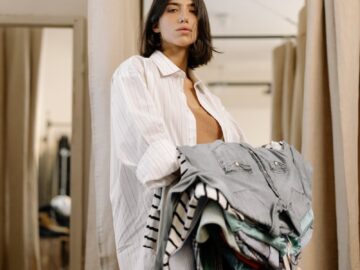 Woman stands in fitting room holding clothes and looking confident in a clothing store.