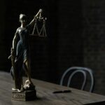 Lady Justice figurine on wooden table in dimly lit room symbolizes law and fairness.