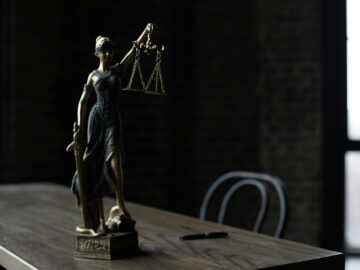 Lady Justice figurine on wooden table in dimly lit room symbolizes law and fairness.