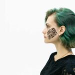 Profile portrait of a young woman with green hair and kinesio tape on her cheek on a white background.
