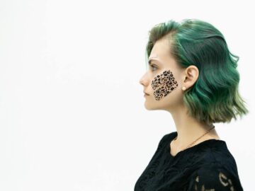 Profile portrait of a young woman with green hair and kinesio tape on her cheek on a white background.
