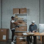 Two male workers organizing and packing boxes in a warehouse setting.