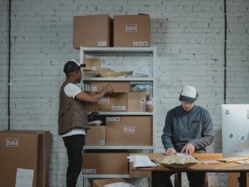 Two male workers organizing and packing boxes in a warehouse setting.