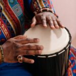 Hands playing a djembe drum, wearing colorful traditional attire, highlighting cultural and musical heritage.