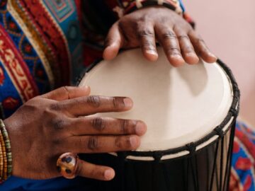 Hands playing a djembe drum, wearing colorful traditional attire, highlighting cultural and musical heritage.