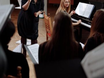 A choir rehearsal indoors with a conductor leading and a pianist accompanying.