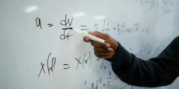 Close-up of hand writing equations on a whiteboard in a classroom setting.