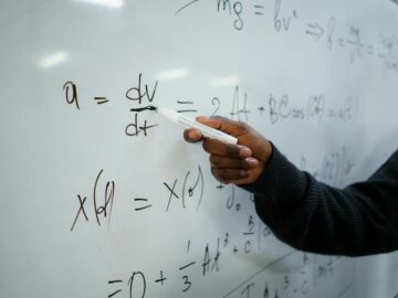 Close-up of hand writing equations on a whiteboard in a classroom setting.