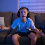 A young boy sitting on a couch, wearing a headset, playing video games indoors.