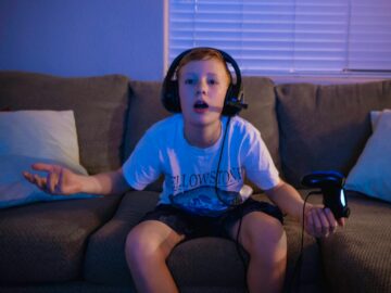 A young boy sitting on a couch, wearing a headset, playing video games indoors.